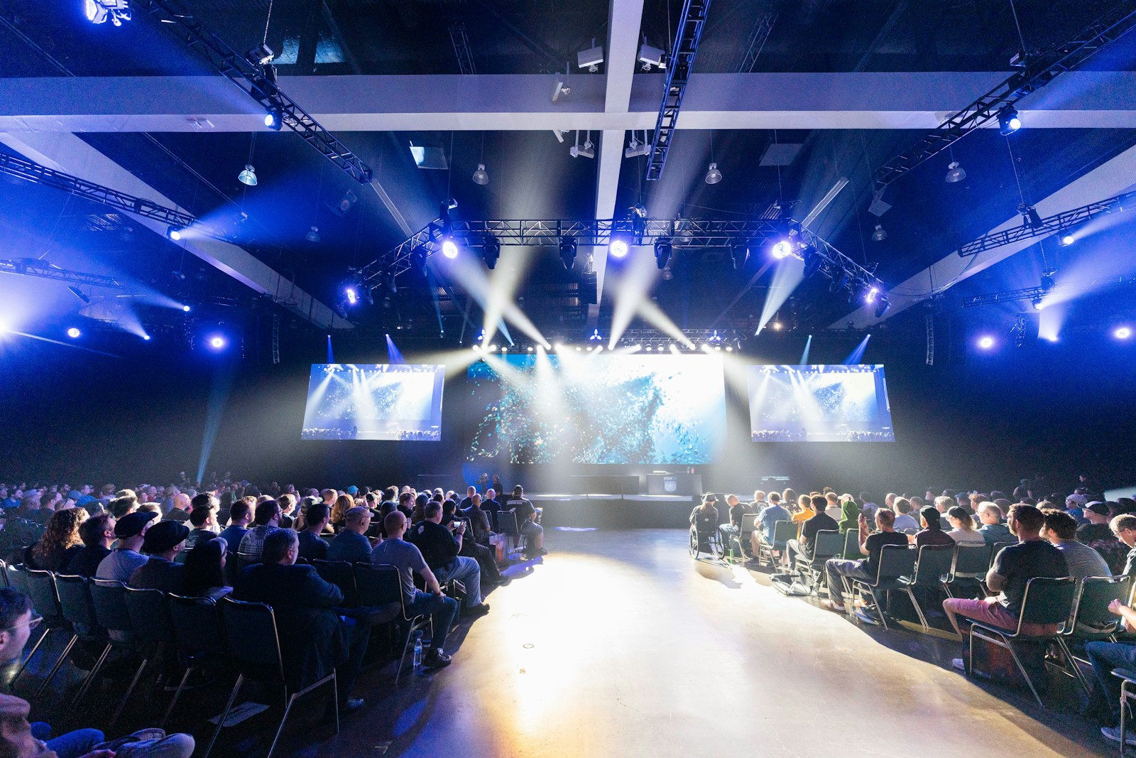 An audience attending a live event with a stage, screens and professional lighting